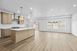 Kitchen featuring backsplash, light countertops, a kitchen island with sink, wall chimney exhaust hood, and light wood-type flooring