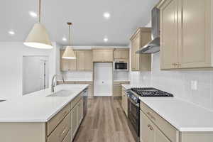 Kitchen featuring appliances with stainless steel finishes, light wood-style flooring, wall chimney range hood, light countertops, and tasteful backsplash