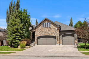 View of front of house with driveway, stone siding, an attached garage, and a front lawn