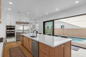 Kitchen with recessed lighting, stainless steel appliances, light wood-style floors, white cabinets, and an island with sink