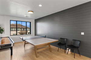 Recreation room with light wood-style floors, a textured ceiling, wood walls, and recessed lighting