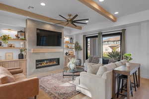 Living area with beamed ceiling, a fireplace, wood finished floors, a ceiling fan, and built in shelves