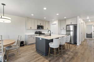 Kitchen featuring appliances with stainless steel finishes, a kitchen island with sink, light wood-style floors, light countertops, and recessed lighting