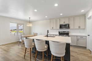 Kitchen with appliances with stainless steel finishes, a kitchen bar, light countertops, recessed lighting, and an island with sink