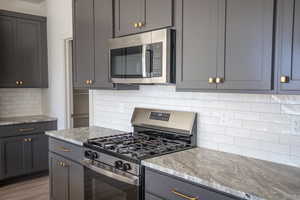 Kitchen featuring appliances with stainless steel finishes, backsplash, gray cabinets, and light stone counters