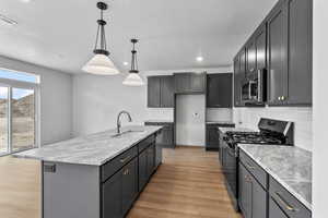 Kitchen with appliances with stainless steel finishes, backsplash, light wood-style flooring, decorative light fixtures, and a center island with sink
