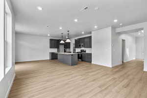 Kitchen with open floor plan, a kitchen island with sink, stainless steel appliances, light wood finished floors, and recessed lighting
