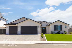 View of front facade with stone siding, a front yard, stucco siding, an attached garage, and decorative driveway