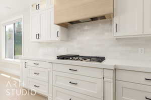 Kitchen featuring light countertops, custom exhaust hood, white cabinets, glass insert cabinets, and stainless steel gas stovetop