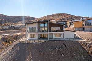 Back of house with a mountain view, a balcony, a patio, and stone siding