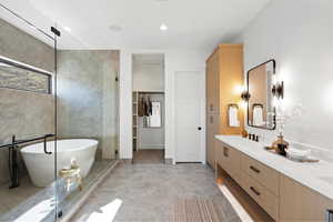 Full bathroom with double vanity, a freestanding bath, a shower stall, recessed lighting, and a walk in closet