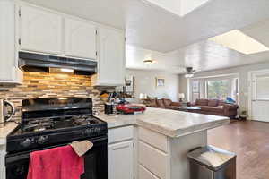 Kitchen with gas stove, a textured ceiling, a peninsula, white cabinetry, and under cabinet range hood