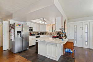 Kitchen with appliances with stainless steel finishes, a peninsula, tasteful backsplash, a textured ceiling, and light countertops