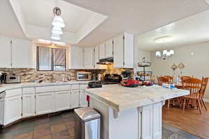 Kitchen featuring a textured ceiling, white cabinets, decorative backsplash, light countertops, and a chandelier