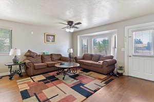 Living room with a textured ceiling, healthy amount of natural light, wood finished floors, and a ceiling fan