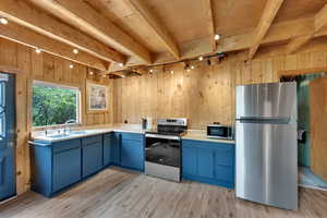 Kitchen featuring track lighting, blue cabinetry, appliances with stainless steel finishes, wood walls, and light wood-style floors