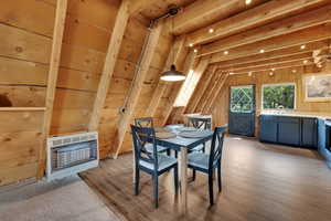 Dining area featuring heating unit, light wood-style floors, wooden walls, and lofted ceiling