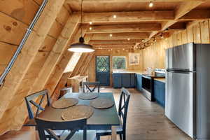 Dining area with light wood-style flooring, wood walls, track lighting, and a wooden ceiling with exposed beams
