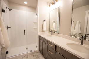 Bathroom with double vanity, light marble finish flooring, a shower stall, and recessed lighting