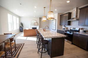Kitchen with stainless steel gas range, a kitchen bar, wall chimney range hood, tasteful backsplash, and open floor plan