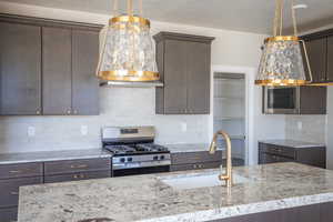 Kitchen with tasteful backsplash, dark brown cabinets, stainless steel appliances, light stone counters, and custom exhaust hood