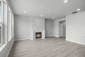 Unfurnished living room featuring light wood-style floors, a warm lit fireplace, and recessed lighting