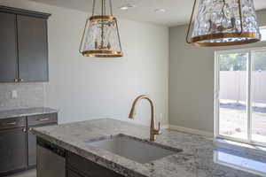 Kitchen featuring light stone counters, stainless steel dishwasher, a chandelier, backsplash, and pendant lighting