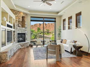 Living room featuring a raised ceiling, hardwood / wood-style floors, a stone fireplace, a ceiling fan, and recessed lighting