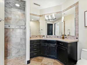 Bathroom featuring vanity, a chandelier, a tile shower, tile patterned floors, and tasteful backsplash