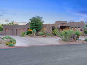Pueblo-style house featuring a garage, driveway, and stucco siding
