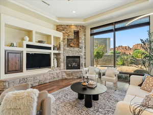 Living area with hardwood / wood-style floors, a stone fireplace, and a raised ceiling