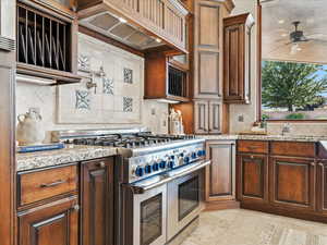 Kitchen with range with two ovens, decorative backsplash, premium range hood, light stone countertops, and light tile patterned floors