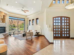 Living room with french doors, wood finished floors, a tray ceiling, a ceiling fan, and a fireplace