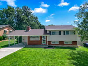 Split level home with driveway, a carport, a front yard, and a chimney