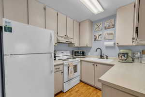 Kitchen featuring white appliances, light countertops, light wood-style floors, and under cabinet range hood
