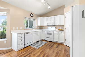 Kitchen featuring white appliances,vaulted ceilings, light wood-style flooring, white cabinets, and light countertops