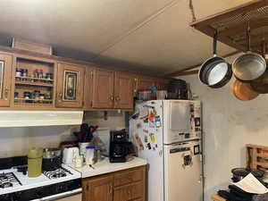 Kitchen with white appliances, brown cabinetry, light countertops, lofted ceiling, and range hood