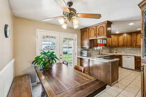 Kitchen featuring tasteful backsplash, french doors, a peninsula, light tile patterned floors, and white dishwasher