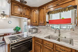 Kitchen with stainless steel range with electric cooktop, brown cabinets, light countertops, and a ceiling fan