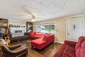 Living room with ornamental molding, wood finished floors, a tile fireplace, a ceiling fan, and a textured ceiling