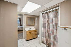 Ensuite bathroom with a paneled ceiling, tile patterned floors, vanity, and curtained shower