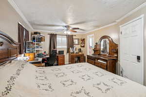 Bedroom with a textured ceiling, ornamental molding, a desk, and a ceiling fan