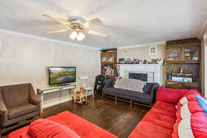 Living room featuring ornamental molding, wood finished floors, a textured ceiling, a tile fireplace, and ceiling fan
