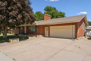 Ranch-style house featuring brick siding, a chimney, concrete driveway, and an attached garage