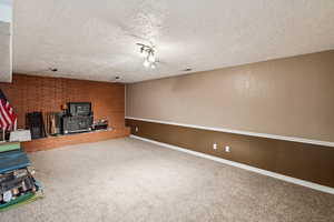 Basement with carpet flooring, a wood stove, a textured ceiling, and brick wall