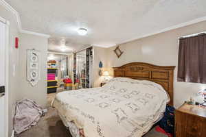 Bedroom featuring a textured ceiling, crown molding, and carpet