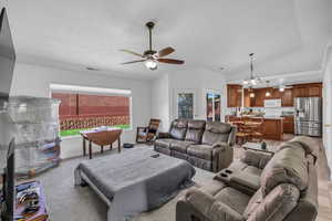 Living area with ceiling fan, healthy amount of natural light, a chandelier, lofted ceiling, and light carpet