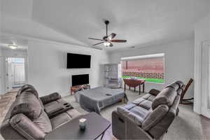 Living room with lofted ceiling, a ceiling fan, a textured ceiling, and light colored carpet