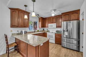 Kitchen with white appliances, a peninsula, light wood finished floors, brown cabinetry, and a textured ceiling