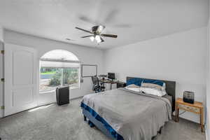 Carpeted bedroom with an office area, a textured ceiling, and a ceiling fan